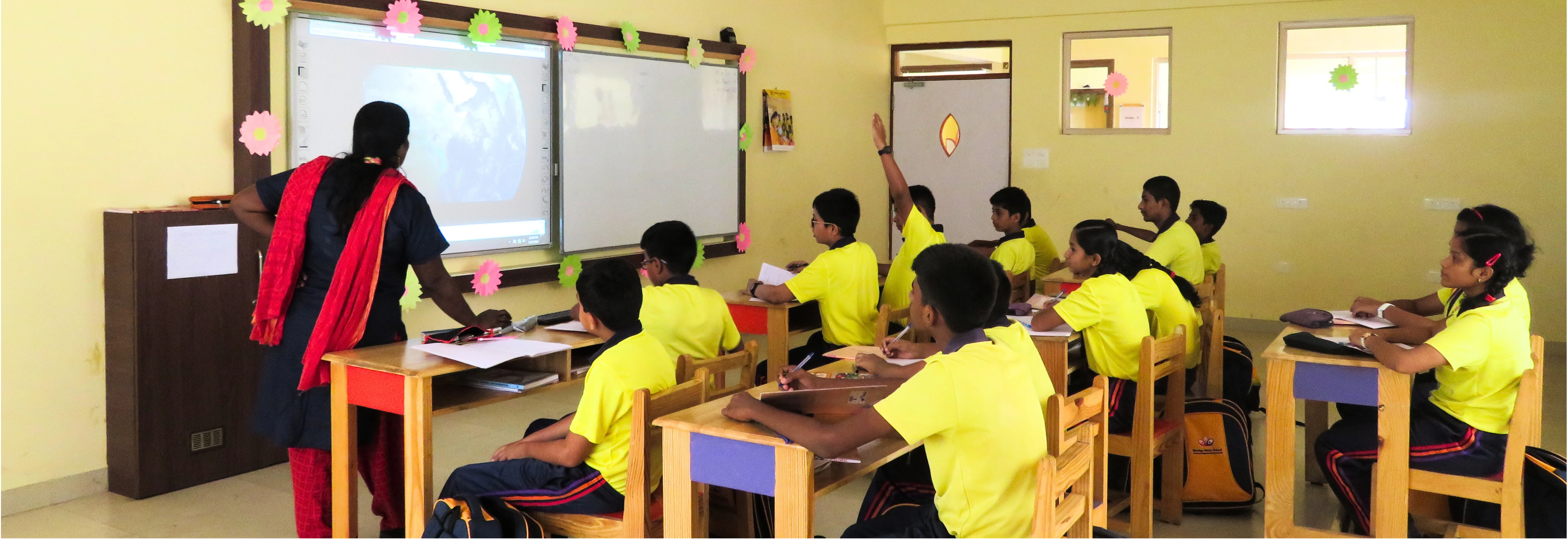 Students at NewAge World School engaged in an interactive classroom session with a teacher using a digital smart board for enhanced learning.